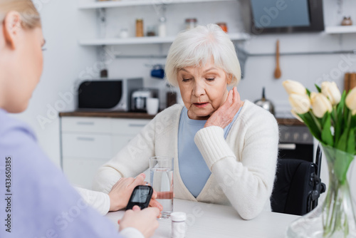 nurse with glucometer touching hand of senior diabetic woman  blurred foreground