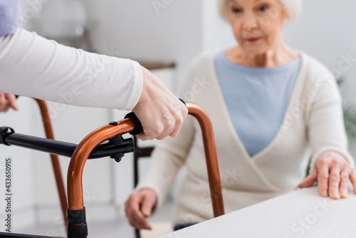 social worker with medical walkers near senior woman sitting on blurred background © LIGHTFIELD STUDIOS