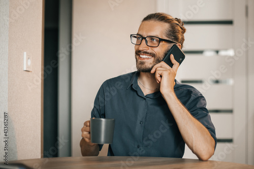 Happy man wearing glasses talking on cell phone at home