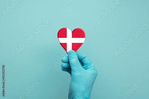 Hands wearing protective surgical gloves holding Denmark flag heart