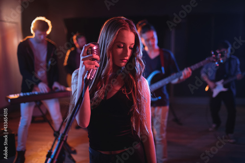Caucasian female singer holding retro microphone at concert in music venue, music band behind her photo