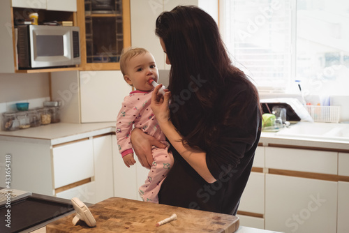 Caucasian baby held and given medication with syringe by mother in kitchen at home