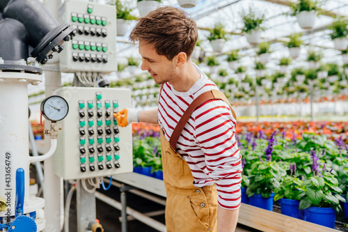 Handsome male experienced plantation worker in overalls equipment with pipelines in modern greenhouse with plants and flowers. Glasshouse pipe heating system photo