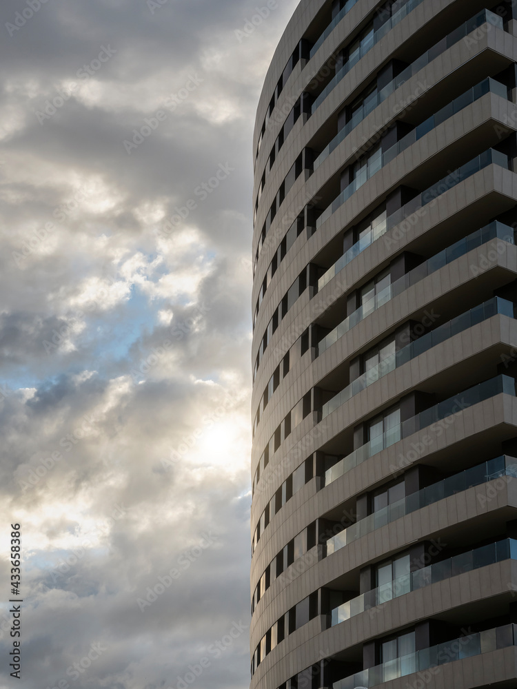 Detail of a facade of a building in an urban area with a cloudy sky in the background at sunset. Reflections and sun glare.