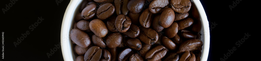White mug filled with coffee beans on a dark background. Fragment. View from above. Web banner White mug filled with coffee beans on a dark background. Fragment. View from above. Web banner