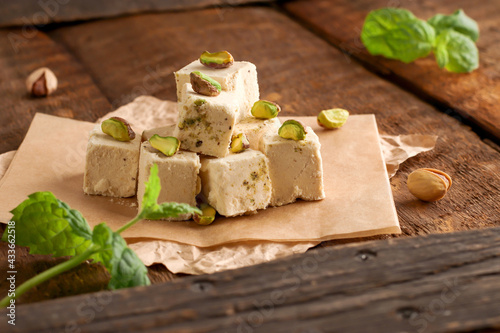 Walnut halva with pistachios on parchment paper on a wooden background. Traditional oriental dessert Chekme. Natural vegan product. Turkish, Arab and Jewish national sweets.