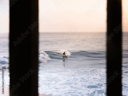 Unrecognizable surfer riding waves of azure sea under clear pink sky in early evening photo