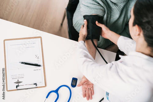 From above of crop unrecognizable female doctor measuring arterial pressure of patient with medical manometer during consultation in hospital photo