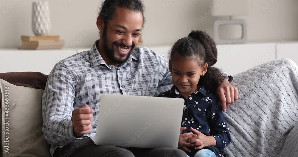 Young African father and little 5s girl using laptop seated on sofa spend time at home with wireless tech, watch cartoons, caring parent teach daughter to use modern device. Weekend leisure concept Young African father and little 5s girl using laptop seated on sofa spend time at home with wireless tech, watch cartoons, caring parent teach daughter to use modern device. Weekend leisure concept