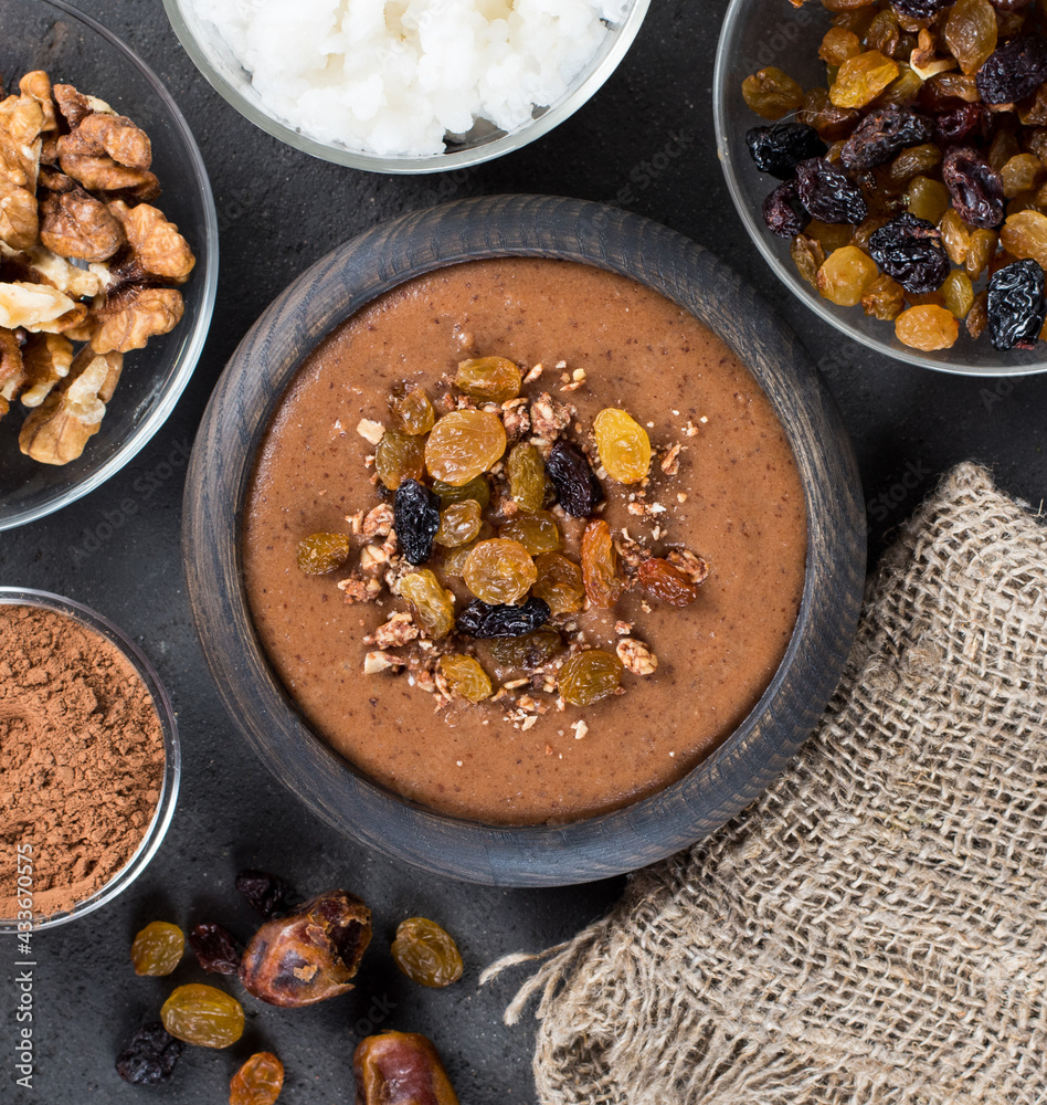 Fototapeta premium Soup puree of dried fruits, raisins, dates, nuts with cocoa in a wooden bowl on a linen napkin on a dark gray background in rustic style top view