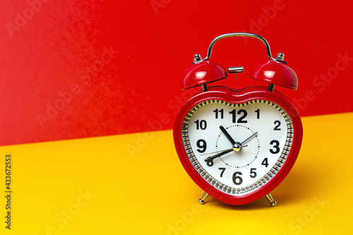 Red metal alarm clock in shape of heart placed on vibrant two colored background in studio photo