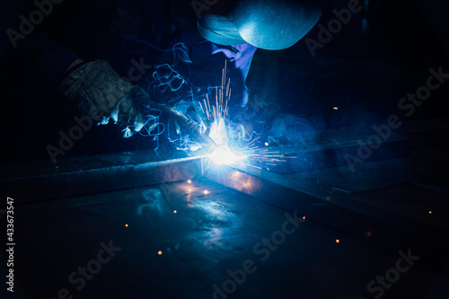 Crop faceless worker in gloves and uniform welding metal details on table near constructions in factory photo