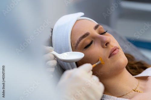 Anonymous crop cosmetologist applying acid peeling on face of female client during visit in beauty clinic