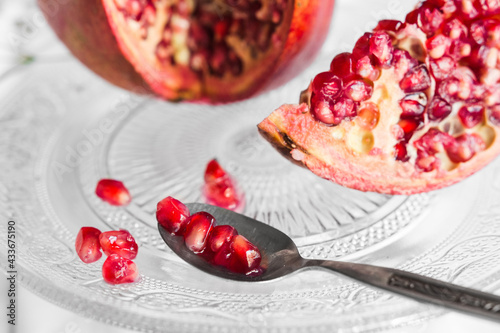 Bright tasty fresh pomegranate with ripe seeds and blooming flower sprig on transparent stand on crumpled fabric