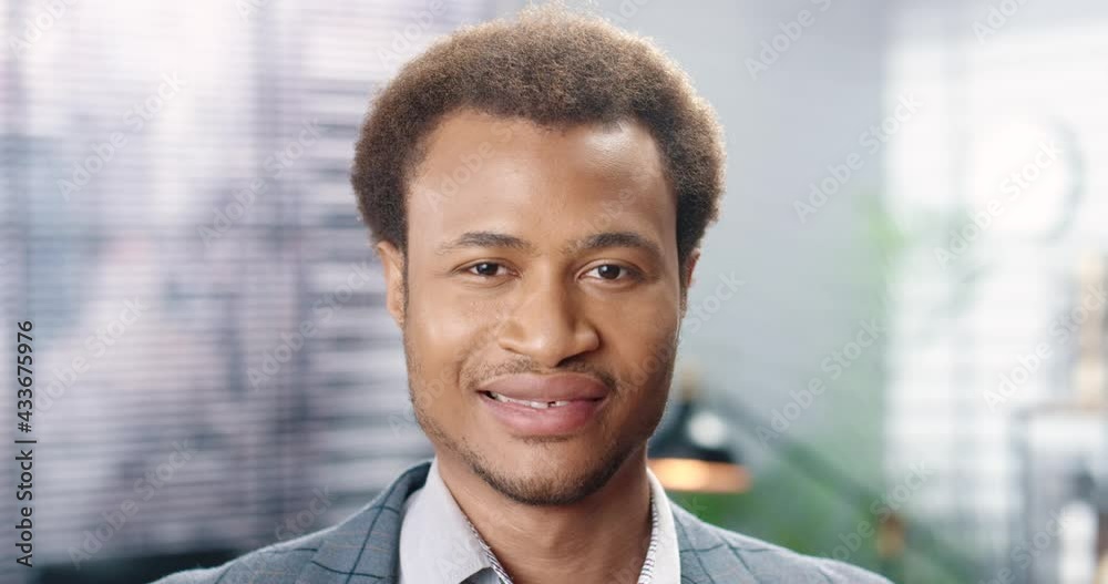 Close up of handsome African American happy young man looking at camera and smiling indoors in good mood. Cheerful male worker with smile on face. Businessman with positive emotions Close up of handsome African American happy young man looking at camera and smiling indoors in good mood. Cheerful male worker with smile on face. Businessman with positive emotions