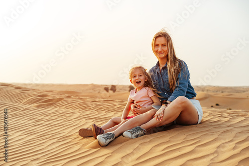 Photography Mother and daughter sitting together on sand dune in the Dubai desert