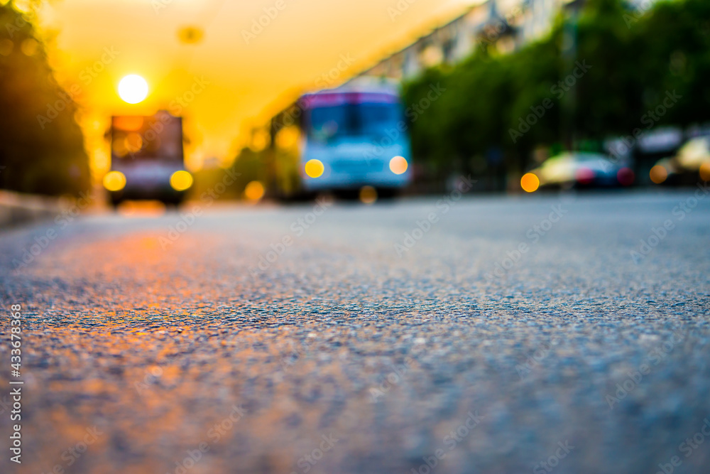 Sunset in the city, the buses driving on the road. Close up view from the asphalt level Sunset in the city, the buses driving on the road. Close up view from the asphalt level