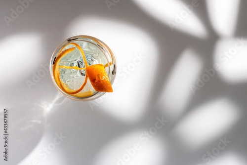 Top view of transparent glass of highball cocktail decorated with citrus fruit zest and clove against shadows in sunlight