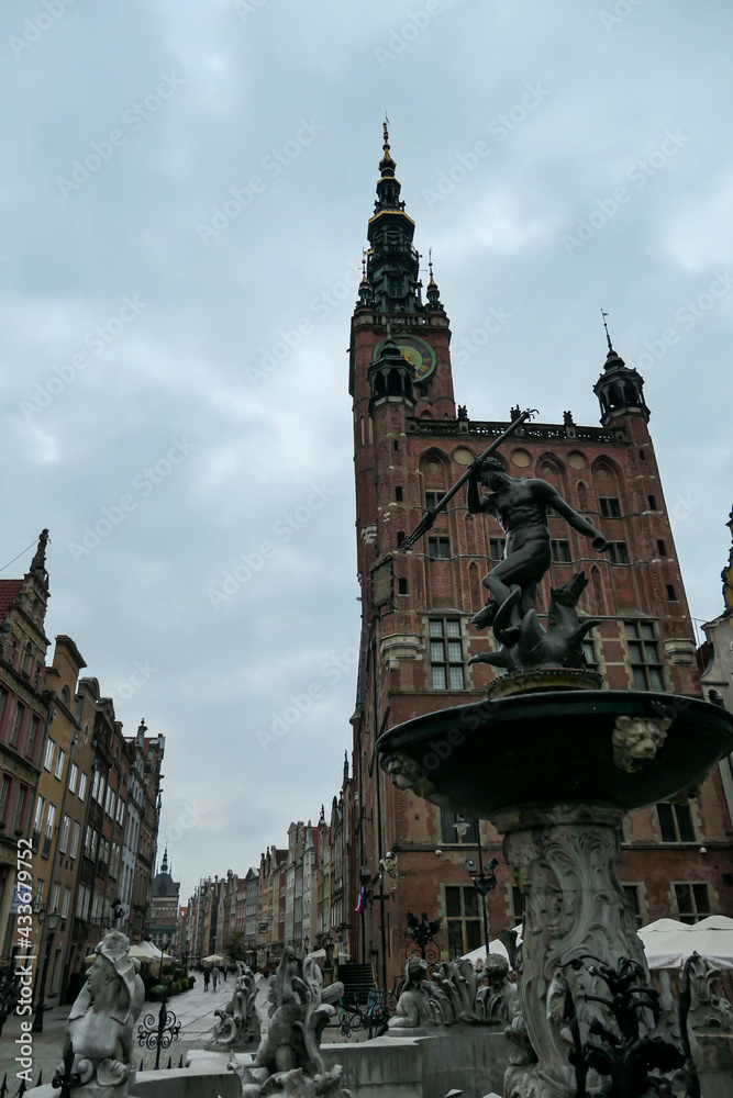 The Neptune's Fountain in Old Town of Gdansk, Poland. The fountain is located in the central point. Red bricked Town Hall building in the back. City tour. A bit of overcast