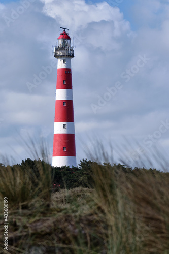 Classic  historic old red and white lighthouse with dunes and grass  sunny windy day and turbulent clouds on the Dutch island of Ameland  Hollum  April 2021