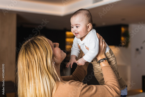 Side view of delighted mother tossing adorable smiling baby while having fun together at home