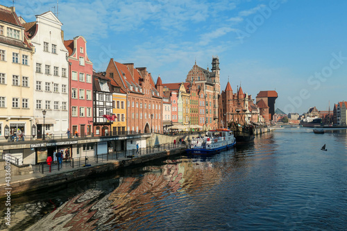 A panoramic view on the shores of Martwa Wisla flowing through Gdansk in Poland, with medieval port crane. New architecture meeting with medieval constructions. Sunny day. Calm water. City tour