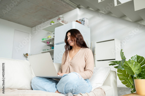 From below woman browsing internet on portable computer while resting on sofa at home