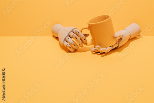 Creative ornamental wooden hand holding colorful mug on yellow background in studio