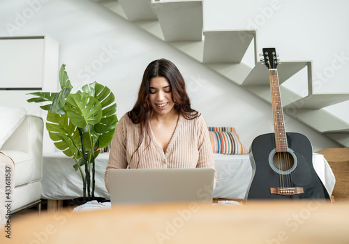 Young glad female browsing internet on portable computer against plant and stairs in house room photo