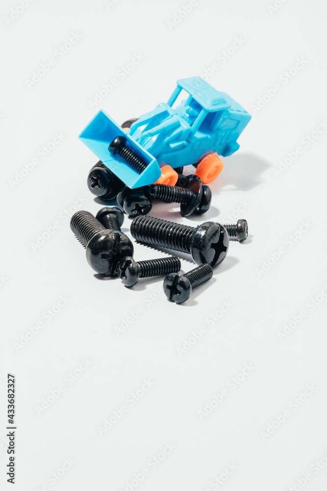 From above of small plastic toy tractor collecting various black screws on white table From above of small plastic toy tractor collecting various black screws on white table