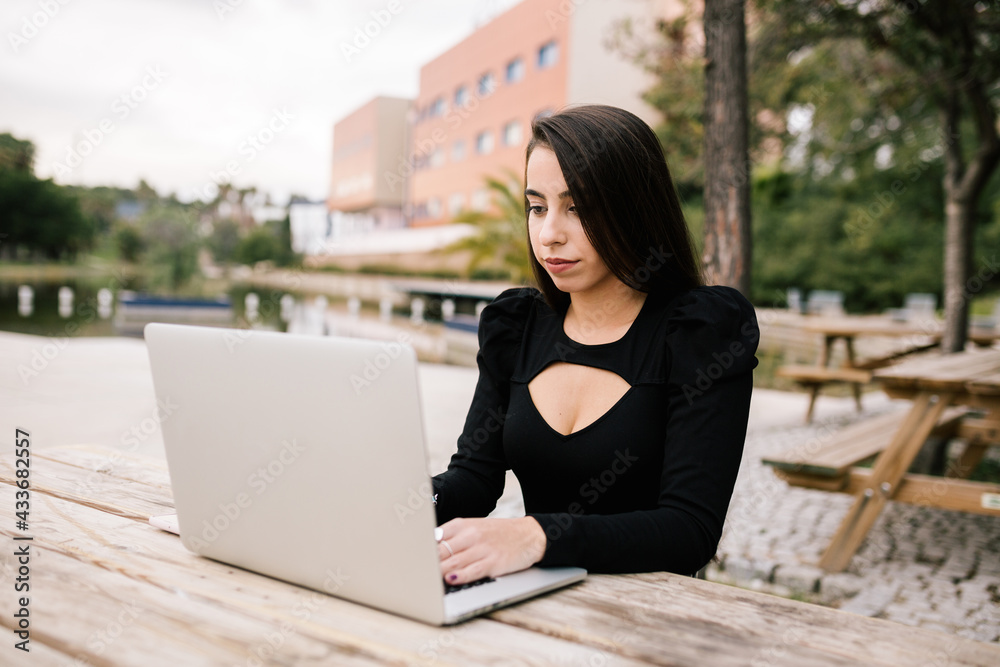 Focused female entrepreneur sitting at table with laptop in park working remotely Focused female entrepreneur sitting at table with laptop in park working remotely