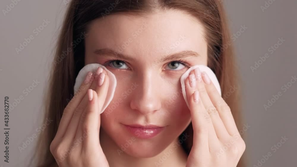Face cleaning. Pretty woman. Perfect makeup. Beauty procedure. Freshness rejuvenation. Smiling lady tenderly touching wiping face with cotton pads isolated beige. Face cleaning. Pretty woman. Perfect makeup. Beauty procedure. Freshness rejuvenation. Smiling lady tenderly touching wiping face with cotton pads isolated beige.