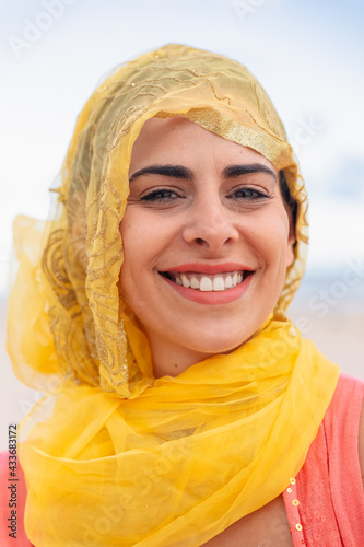 Young glad female with toothy smile looking at camera on blurred background of cloudy sky