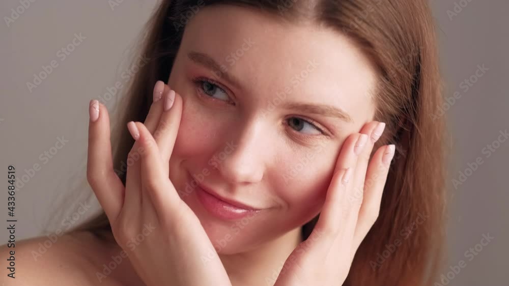 Facial care. Female beauty procedure. Smooth skin treatment. Lifting massage. Pretty smiling woman tenderly touching face after applying cosmetic isolated beige. Facial care. Female beauty procedure. Smooth skin treatment. Lifting massage. Pretty smiling woman tenderly touching face after applying cosmetic isolated beige.