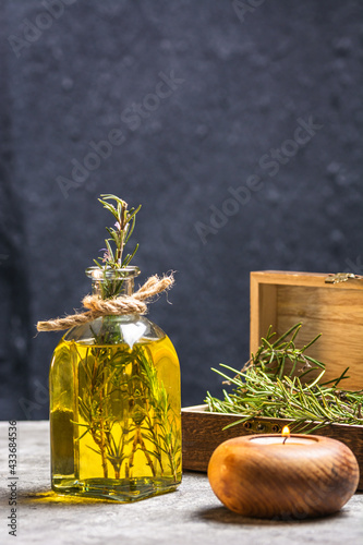 Glass bottle of essential oil with rosemary twigs and burning organic wooden candle on gray table photo