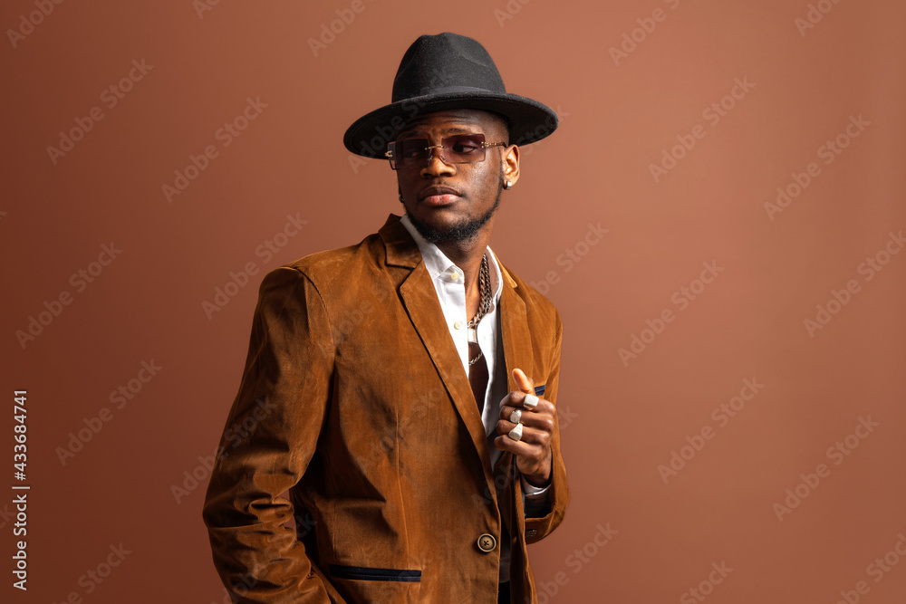 Young African American male in trendy apparel and hat looking away on brown background Young African American male in trendy apparel and hat looking away on brown background