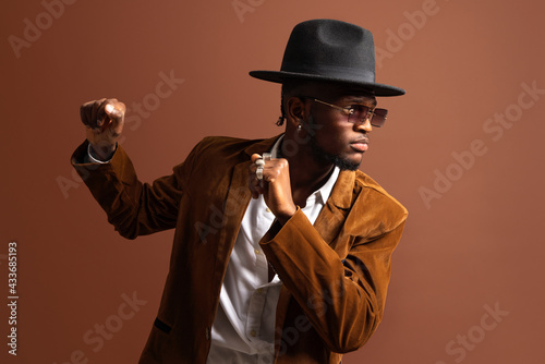 Young African American male in trendy apparel and hat dancing looking away