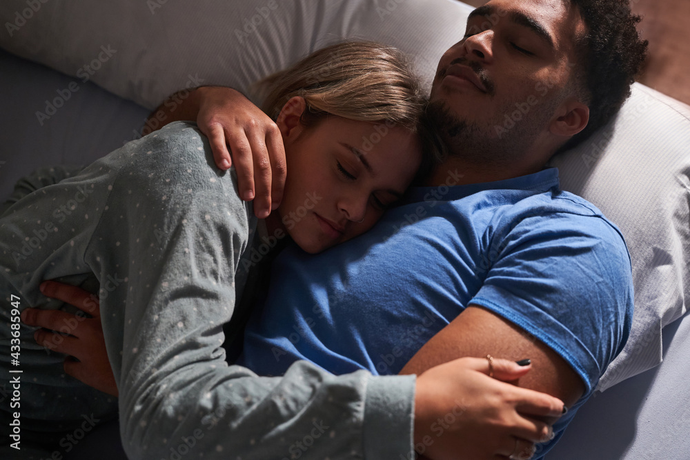 From above of serene multiethnic couple lying on bed and embracing while sleeping in cozy bedroom From above of serene multiethnic couple lying on bed and embracing while sleeping in cozy bedroom