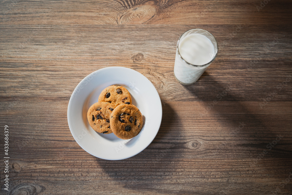 From above of plate with tasty oatmeal biscuits with chocolate chips against glass of milk on wooden table From above of plate with tasty oatmeal biscuits with chocolate chips against glass of milk on wooden table
