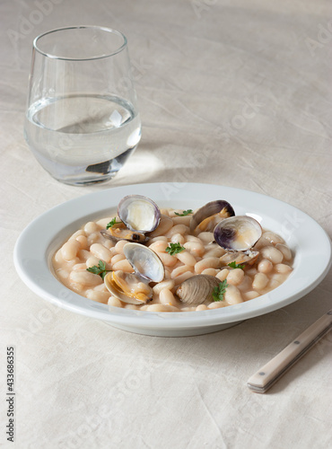 Appetizing traditional spanish stewed white fabes beans with mollusks in plate with fresh parsley leaves on tablecloth photo