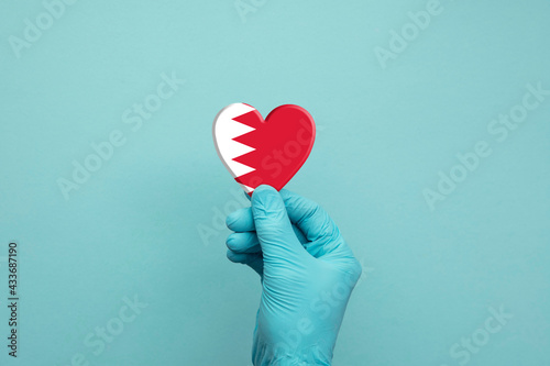 Hands wearing protective surgical gloves holding Bahrain flag heart
