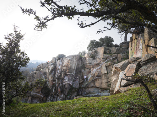 Back view full body of painter with spray paint making graffiti hanging on rope on steep rocky slope