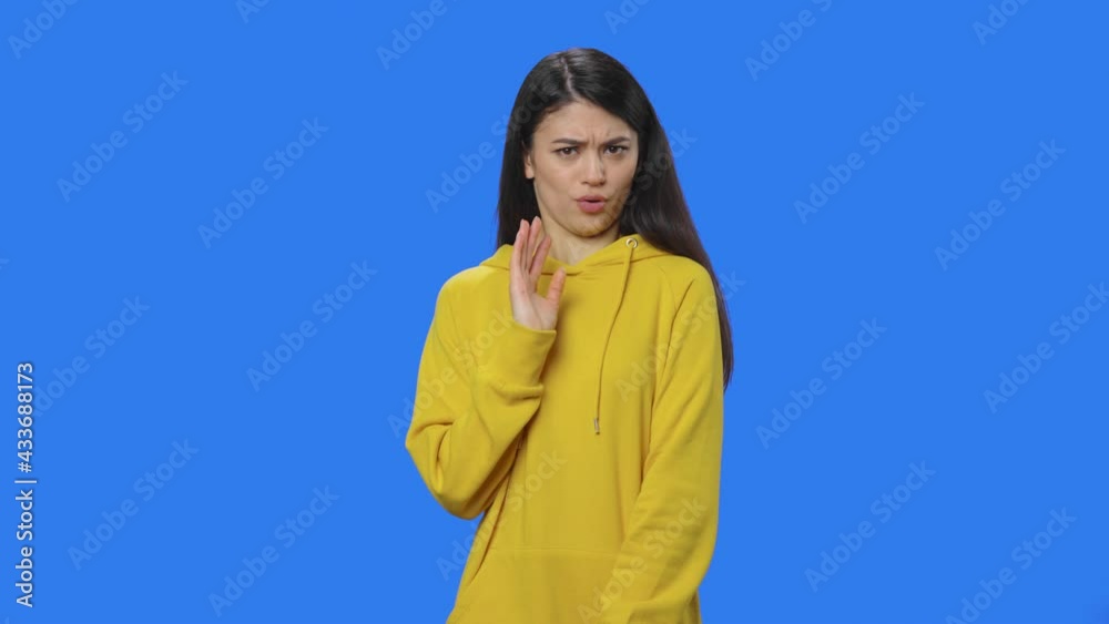 Portrait of pretty brunette pointing herself, say who me no thanks i do not need. Young woman in yellow sweatshirt posing in studio with blue screen background. Close up. Slow motion ready 59.94fps.