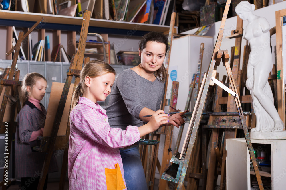 Fototapeta premium Smiling woman teacher correcting work of girl during painting class at art studio