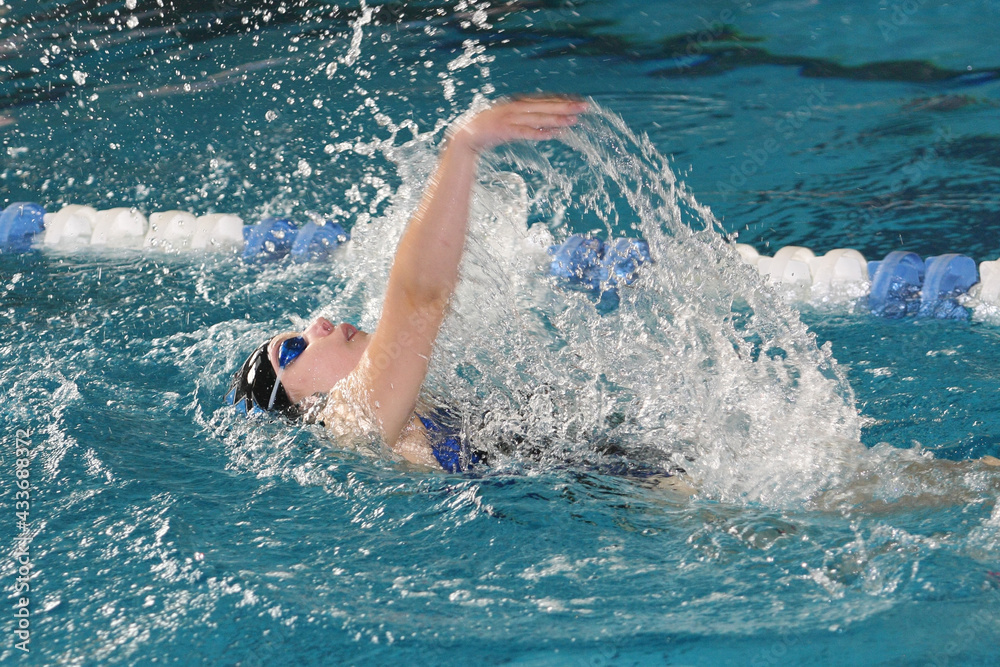 teenage girl swimming in swim meet doing backstroke
