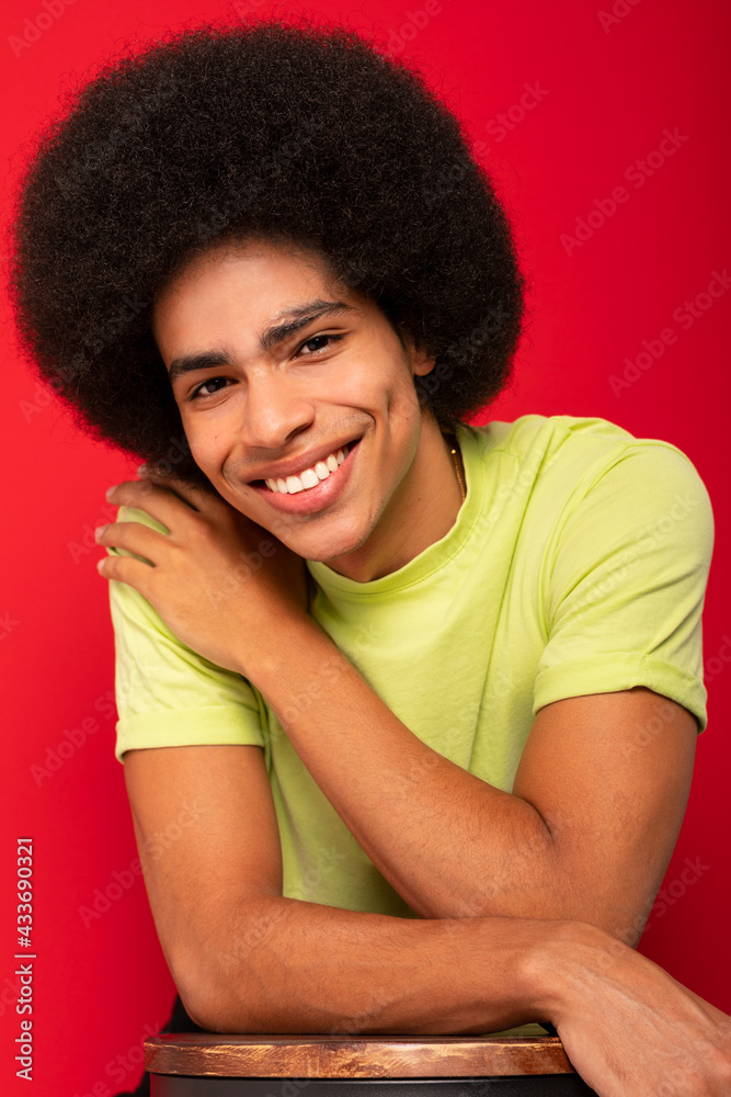Young self cheerful African American male in casual t shirt looking at camera on red background Young self cheerful African American male in casual t shirt looking at camera on red background