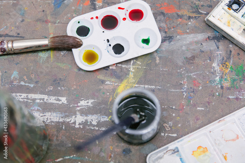 Top view of paintbrushes and paint palettes arranged on table with jar of water in art studio photo