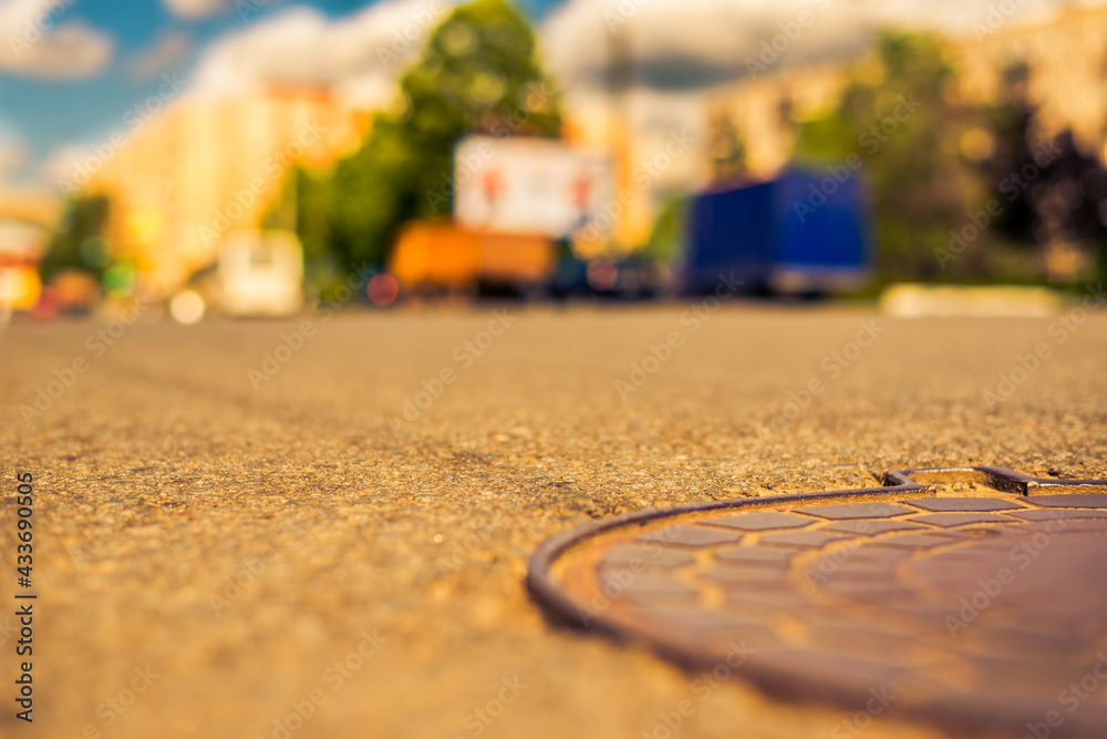 Obraz premium Summer in the city, the cars passing by on the street. Close up view of a hatch at the level of the asphalt