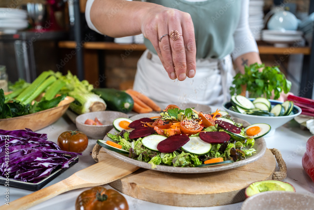 Crop anonymous female preparing delicious vegetable salad with sesame seeds at table in house kitchen