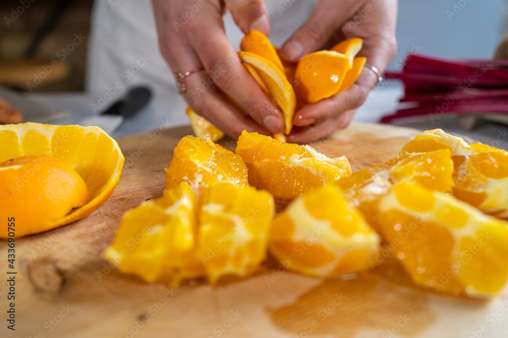 Crop unrecognizable female peeling ripe juicy oranges on wooden chopping board at kitchen table Crop unrecognizable female peeling ripe juicy oranges on wooden chopping board at kitchen table